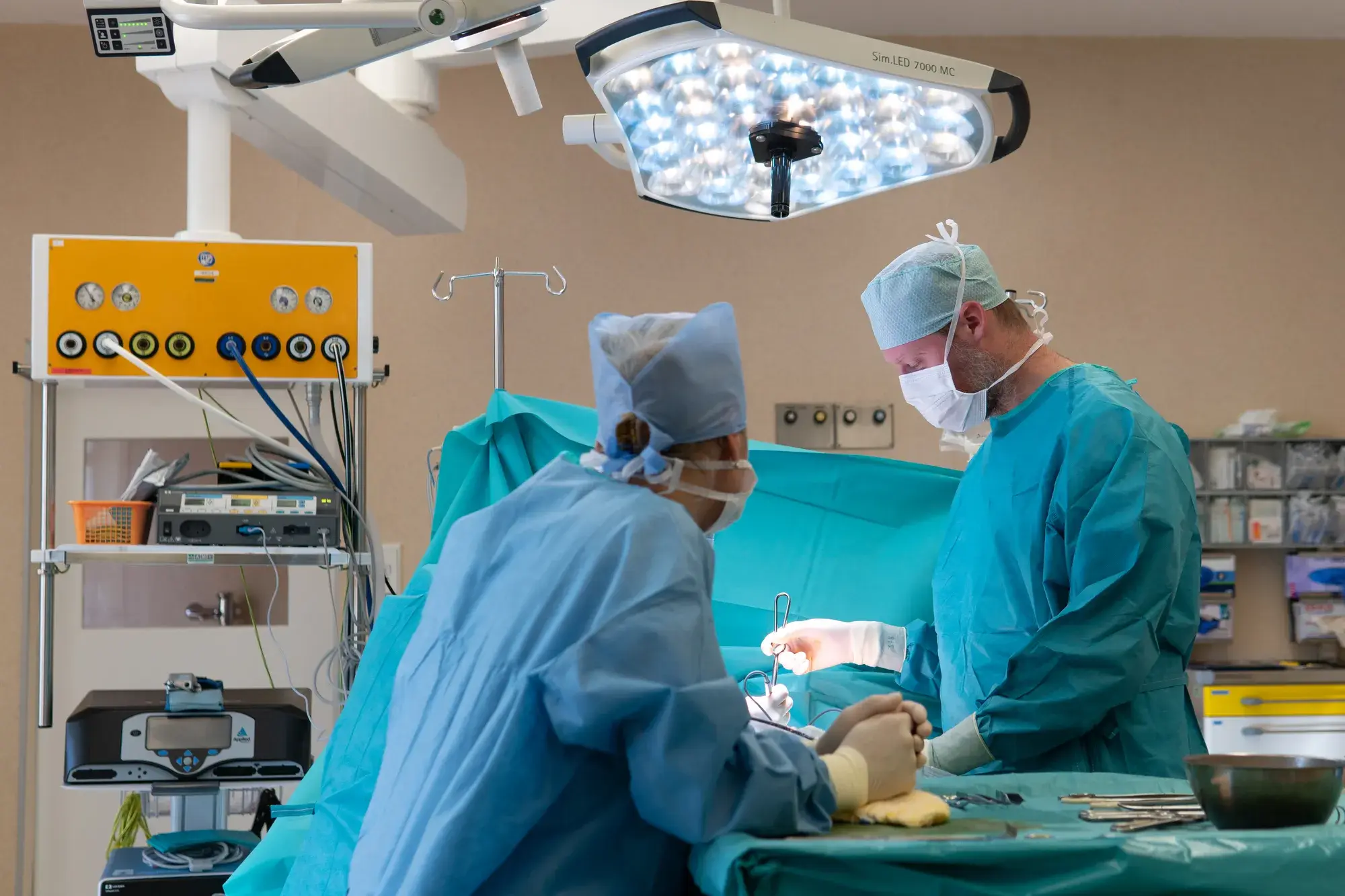 Operace na sále, chirurgové u operačního stolu pod lampami