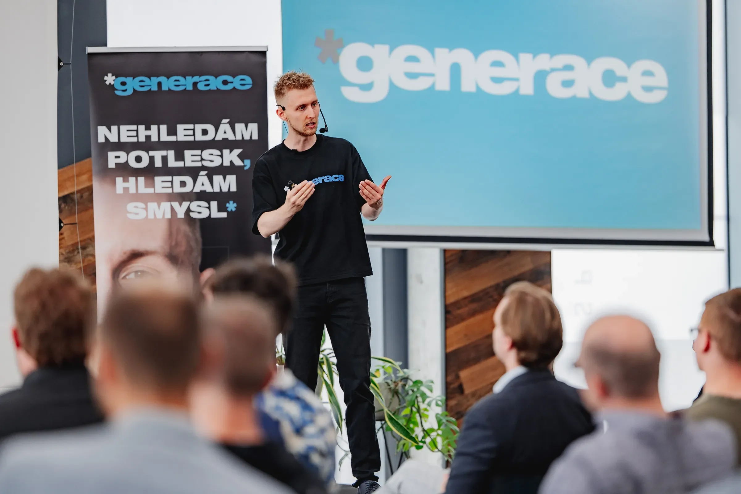 Daniel Krutý mluví na pódiu před plátnem s logem Generace